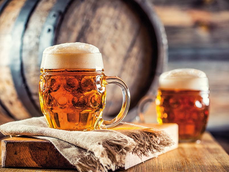 Glasses of beer in a brewery sitting in front of a wooden keg